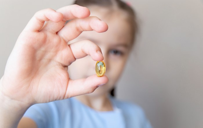 A child holding up an omega-3 supplement.