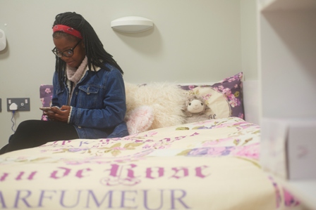 A female student sitting on her double bed in her student room and looking at her phone