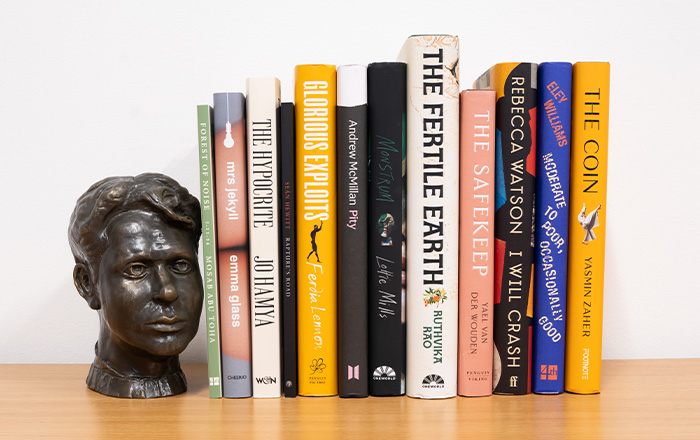 Bookshelf image of the 12 book spines accompanied by bronze bust of Dylan Thomas