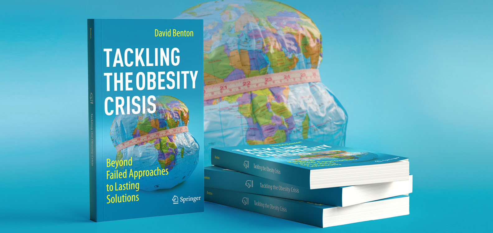 Copïau o lyfr newydd yr Athro David Benton, Tackling the Obesity Crisis: Beyond Failed Approaches to Lasting Solutions. Yn y cefndir, ceir graffigyn o glôb chwyddadwy sydd â thâp mesur o'i amgylch.