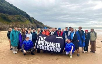 Students holding a Movember flag after their cold sea dip for charity 