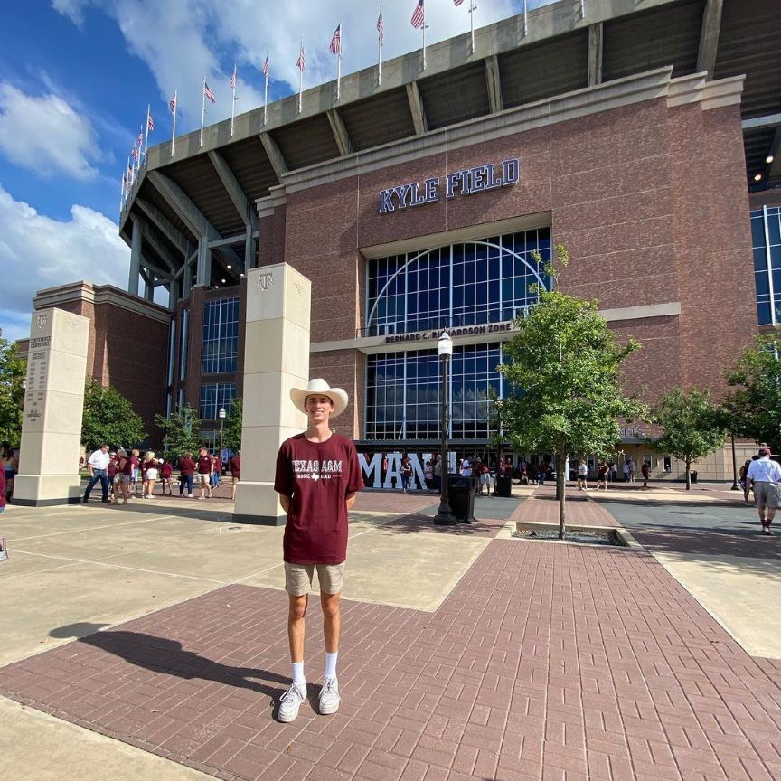 STUDENT IN TEXAS A&M TSHIRT STANDING IN FRONT OF BUILDING