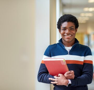 A student holding a library book with bookshelves in the background