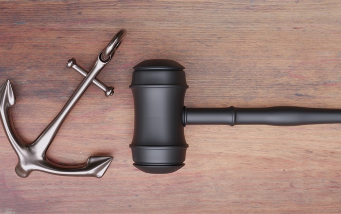 A small silver anchor and black gavel on a wooden background