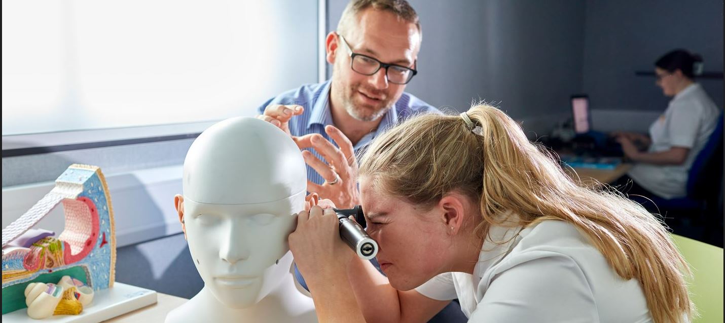 Student studying an audiology anatomy model with lecturer instructing